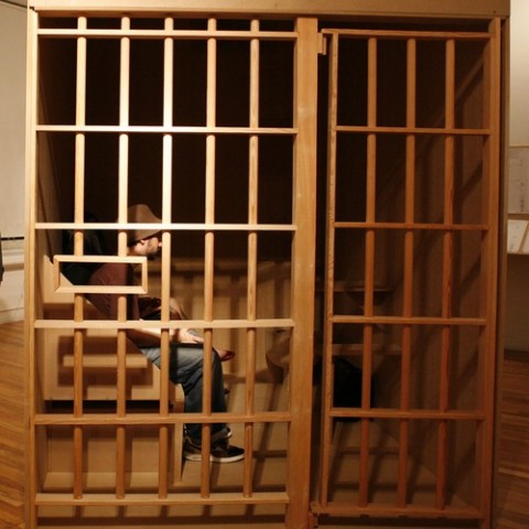 A man sits in a model of Herman's cell at The House That Herman Built art exhibit. (Photo: http://hermanshousethefilm.com/)