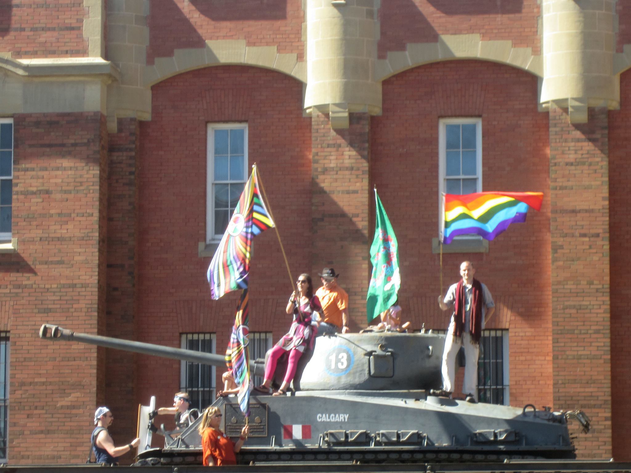 Gay Pride marchers wave rainbow flags atop Calgary's Mewata Armoury tank