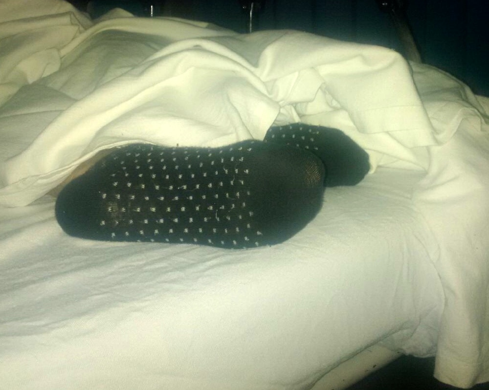 Woman's feet under a rumpled sheet on a stretcher in an emergency department.