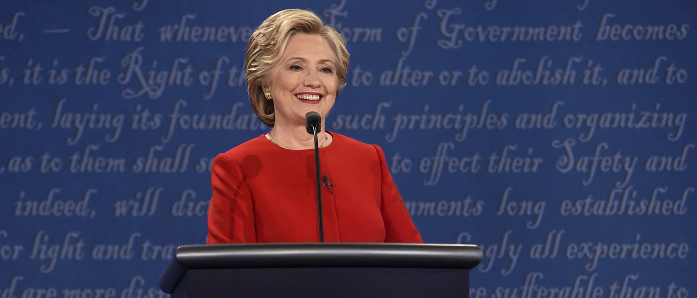 Hillary Clinton in a bright red top against the blue debate background.