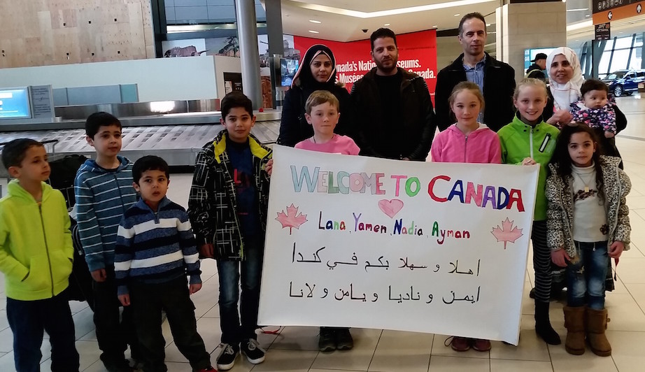 Dima Siam (far right, in white hijab, holding her baby, Maria), welcomes her brother-in-law and his family as sponsored refugees to Canada on April 12. Siam is fighting a deportation order that would send her to Syria, the result of a simple paperwork error. The Trudeau government has thus far refused to end her nightmare of limbo and grant her permanent resident status.  Credit: Brian Cornelius