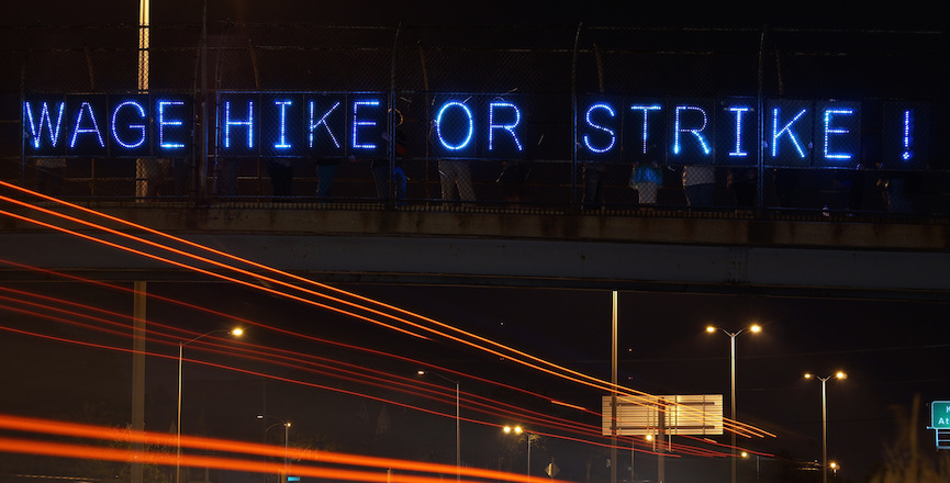 Neon "Wage Hike or Strike" sign above traffic. Image: Flickr/Joe Brusky