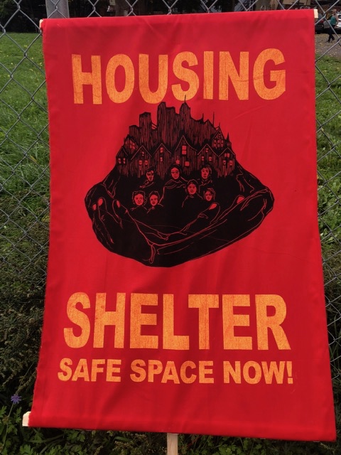 A protest banner with words Housing Shelter Safe Space Now