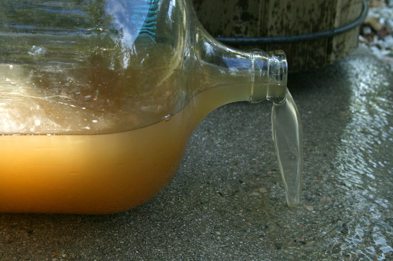 Dirty water spilling out of a large glass carboy on its side. Photo by Ildar Sagdejev/ Wikimedia Commons.