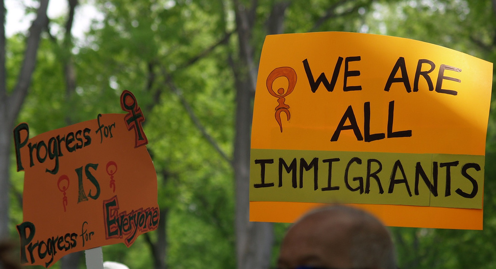 Person holds sign reading "We are all immigrants." Photo: takomabibelot/Flickr