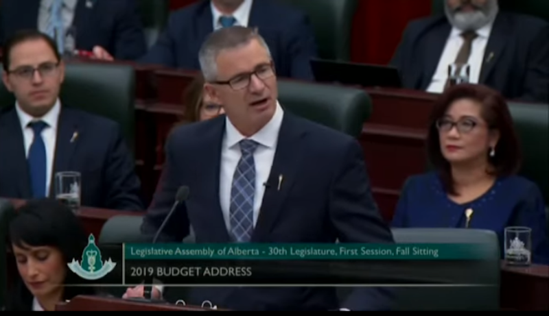 Alberta Finance Minister Travis Toews reads the province’s budget speech yesterday. Image: Screenshot of Government of Alberta video