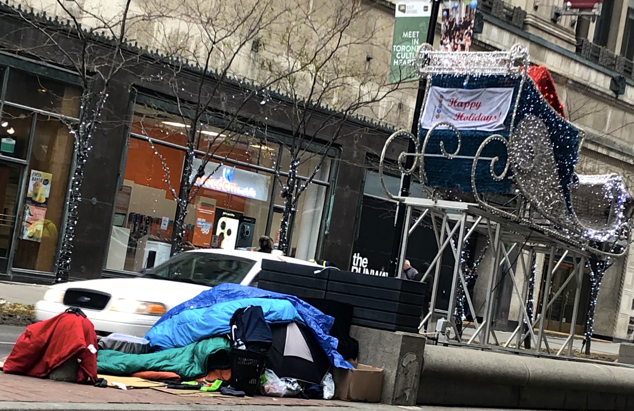 A homeless person sleeps next to Santa's sleigh on a main street in Toronto. Image: Cathy Crowe