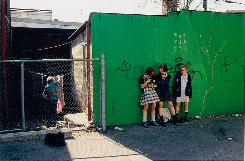 Three_women_standing_against_a_wall