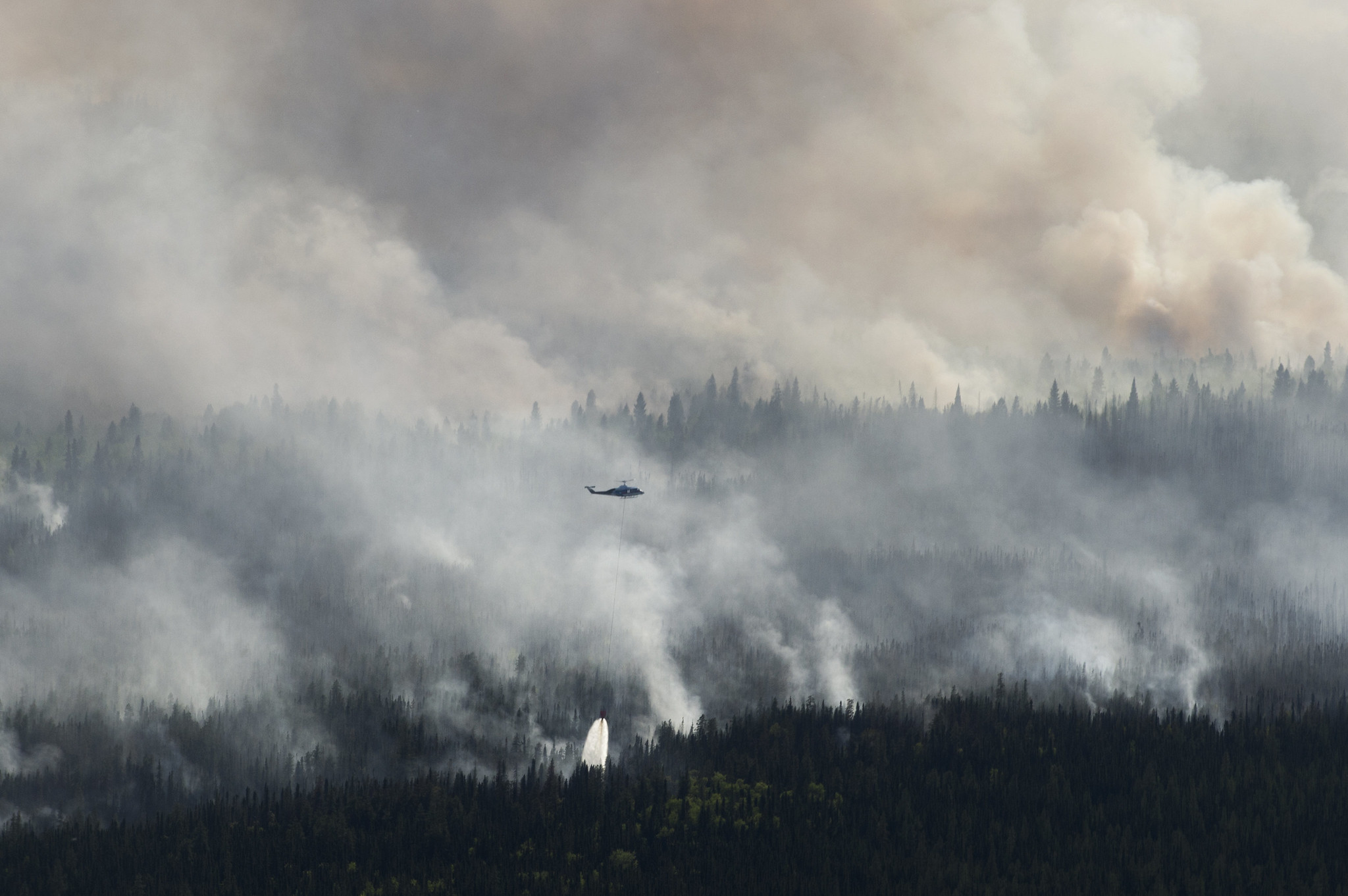 A helicopter drops a bucket of water on a wildfire near High Level, Alberta in May 2019. Image: Chris Schwarz for Government of Alberta/Flickr