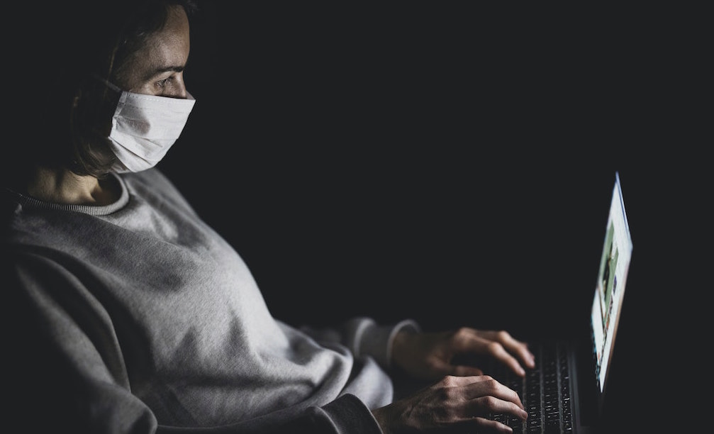 Person wearing face mask using laptop computer. Image credit: engin akyurt/Unsplash