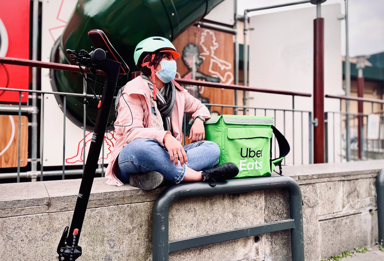 Person wearing bicycle helmet sits next to Uber Eats box. Image credit: Sargis Chilingaryan/Unsplash