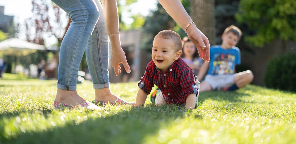 Person supervises baby crawling on grass. Image credit: Jordan Rowland/Unsplash