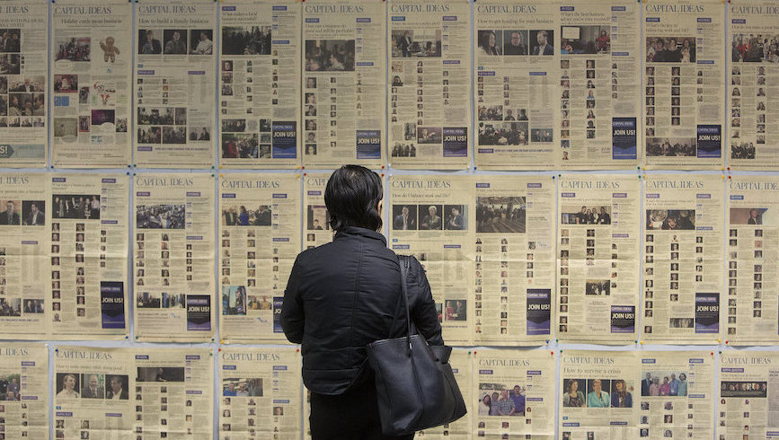 Person stands in front of display of newspaper broadsheets. Image credit: Jason Franson/ Postmedia via Capital Ideas Edmonton/Flickr