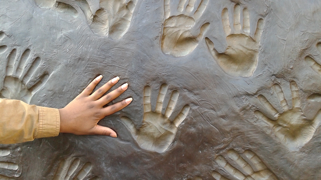 A nursing student's hand reaches out to touch the imprint of hands in a sculpture at a community drop-in centre. Image credit: Cathy Crowe