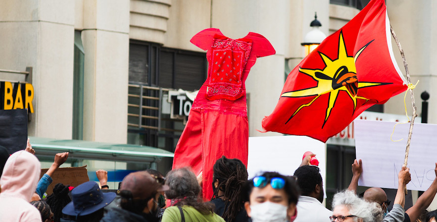 Large crowd of protesters on the streets of Toronto. A red dress and Mohawk Warrior flag can be seen hoisted above the crowd. May 30, 2020, by Louis Karoniaktajeh Hall.