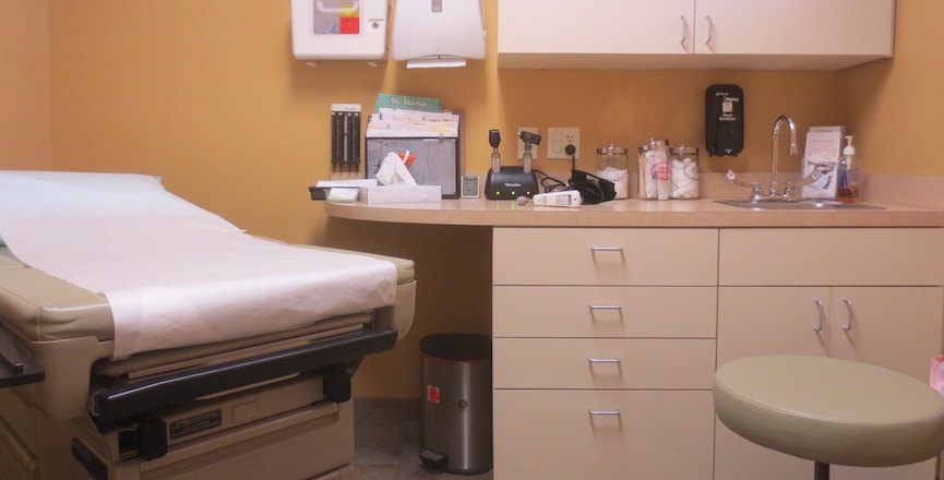 A doctor's office with an exam bed, a stool, and a counter with medical supplies. Image: TheKarenD/Flickr