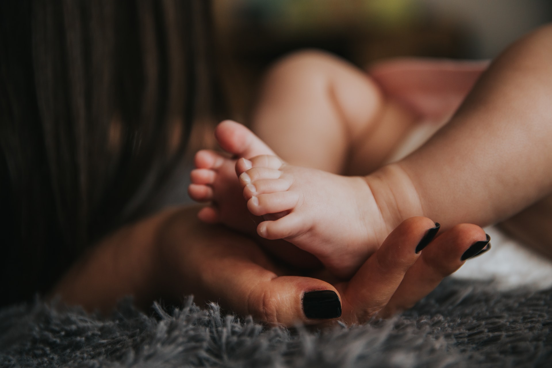 A hand with black nail polish supports a baby's feet. Image: Alex Pasarelu/Unsplash