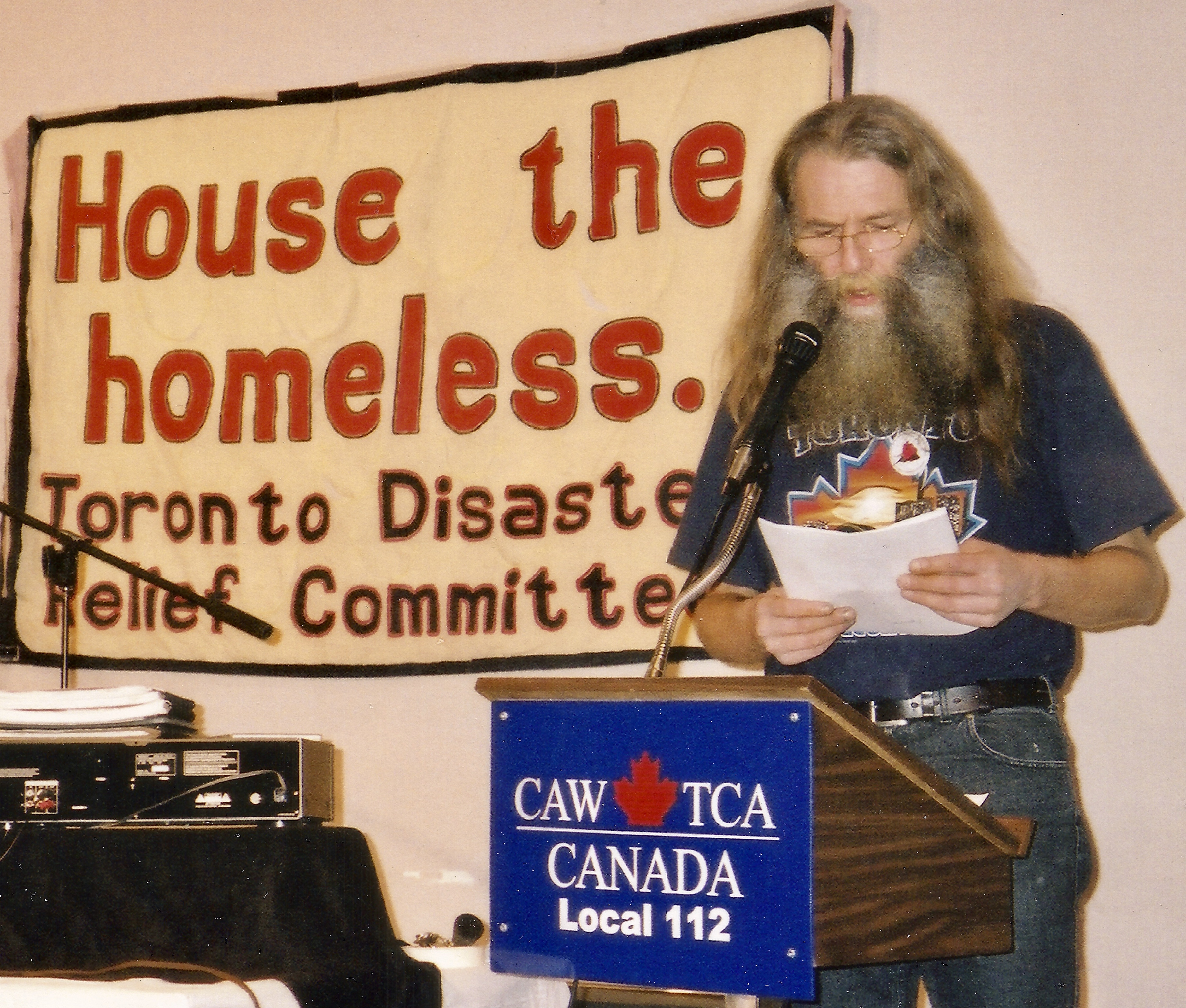 Dri, from Tent City, speaks at a CAW podium in front of a TDRC banner that says House the Homeless. Image: Cathy Crowe/Provided