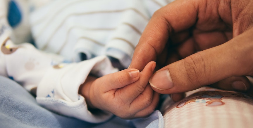 A baby's hand is held by another hand. Image: Aditya Romansa/Unsplash