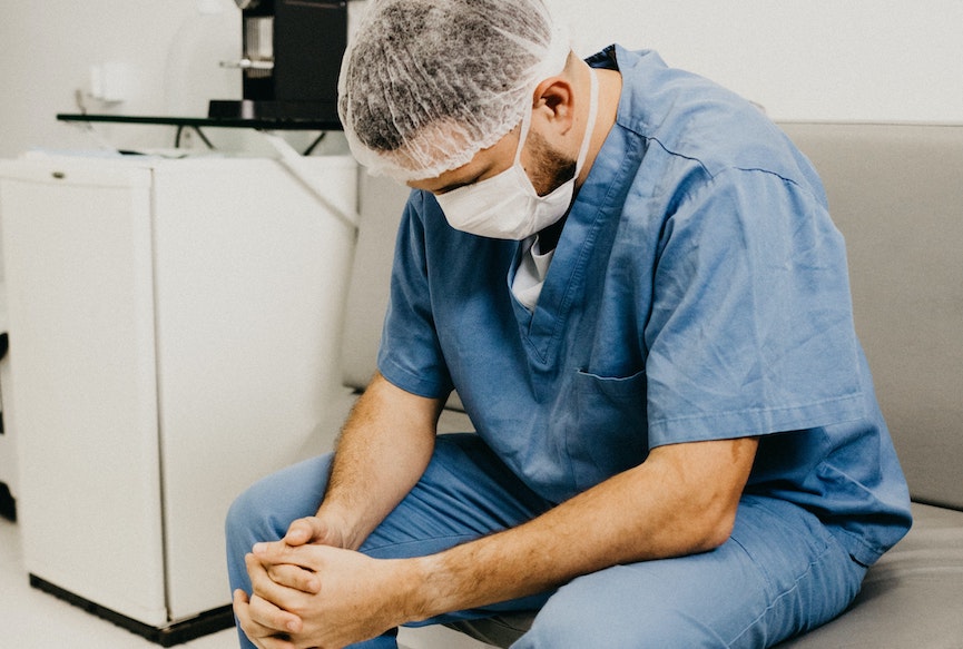 A healthcare worker hangs their head and looks at their hands. Image: Jonathan Borba/Unsplash