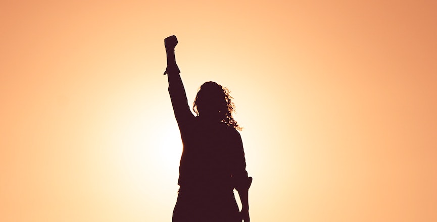 The silhouette of a woman with her fist raised in the air. Image: Miguel Bruna/Unsplash