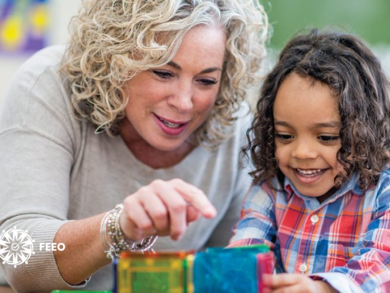 Photo of a white woman and a racialized child smiling and playing with blocks