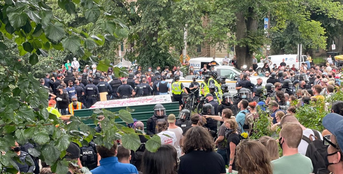 Police tear down an encampment in a Halifax park as protestors look on, August 18 2021. (Image: Kate Higginson/Used with permission)