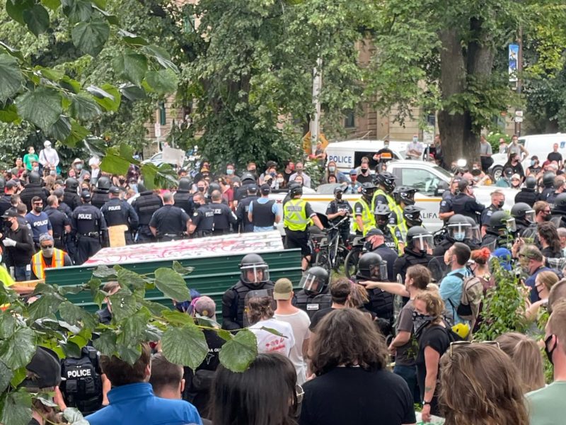 Police tear down an encampment in a Halifax park as protestors look on, August 18 2021. (Image: Kate Higginson/Used with permission)