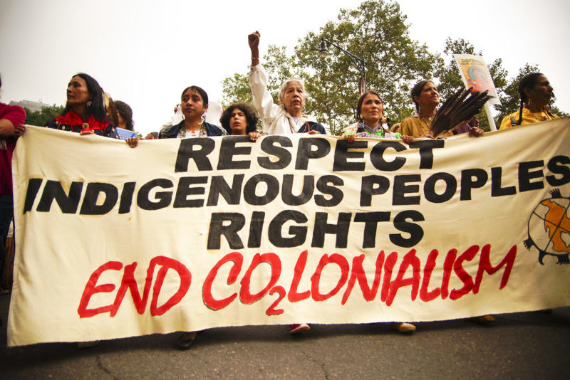 Photo of a protest with a banner reading "respect indigenous peoples rights. End colonialism."