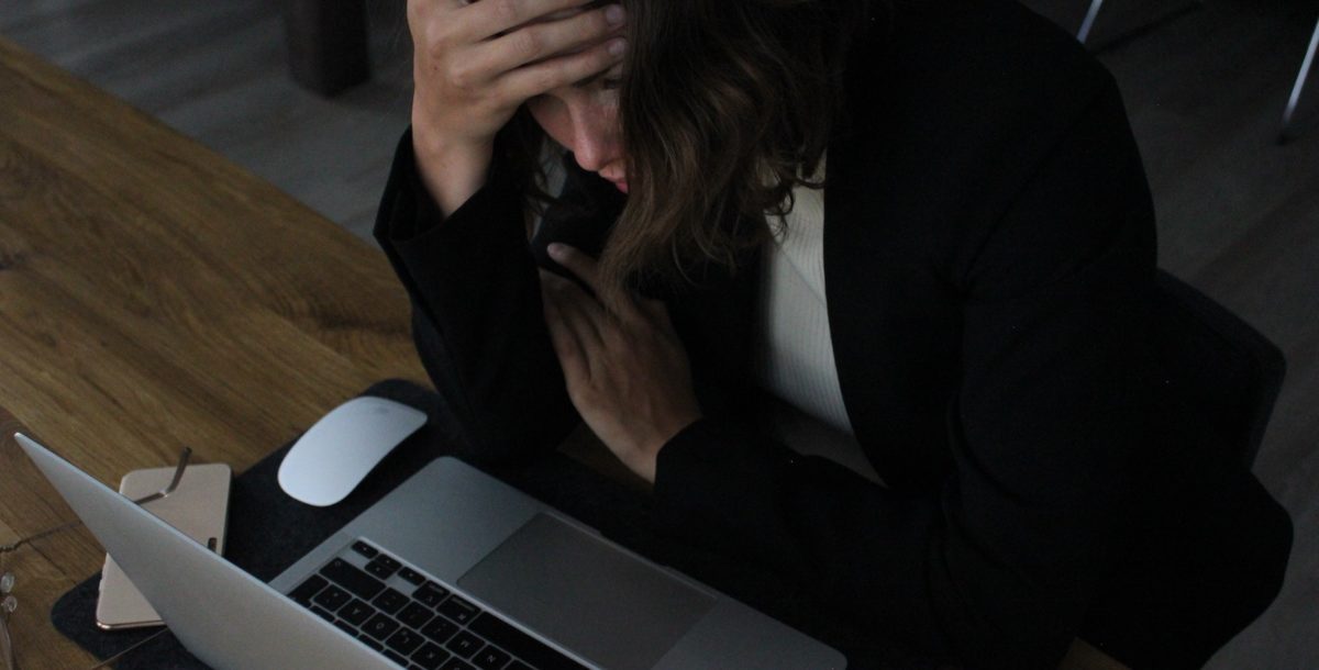 A woman sits in front of a laptop with her head in her hands. (Image: Elisa Ventur/Unsplash)