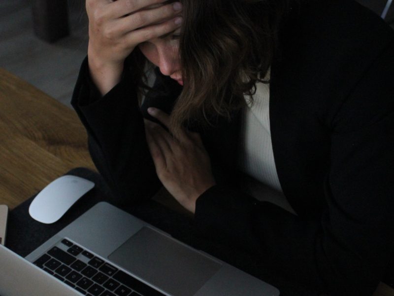 A woman sits in front of a laptop with her head in her hands. (Image: Elisa Ventur/Unsplash)