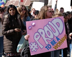 Photo of a woman holding a sign reading Proud to be a woman