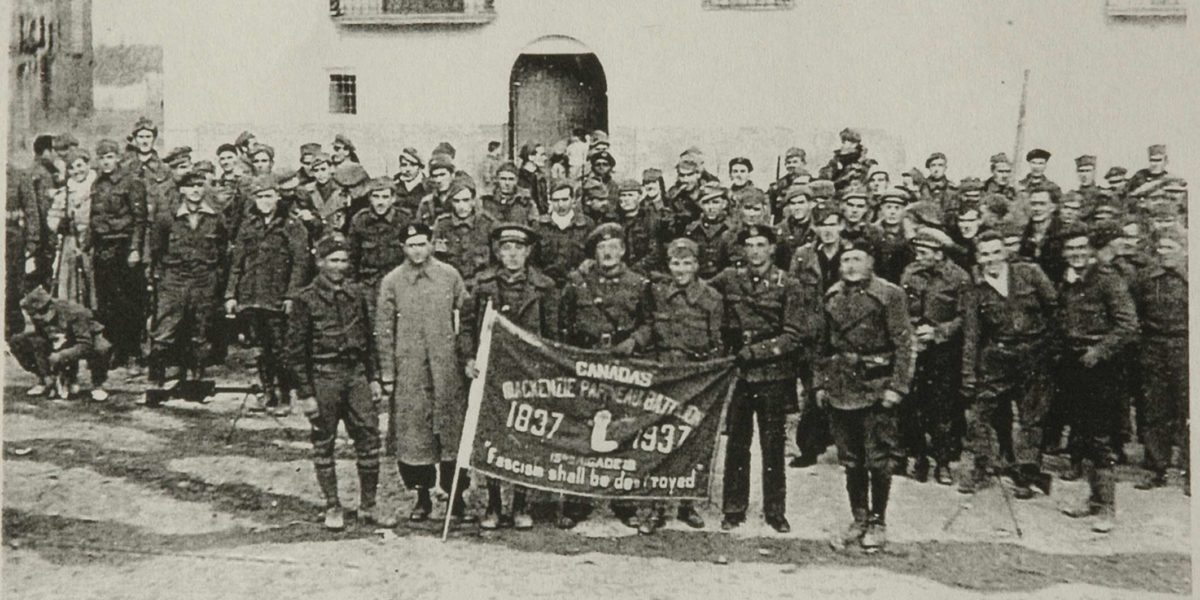 Group photo of the Mackenzie Papineau Battalion holding their unit flag.