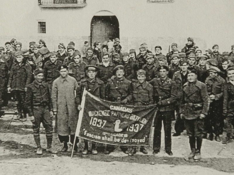 Group photo of the Mackenzie Papineau Battalion holding their unit flag.