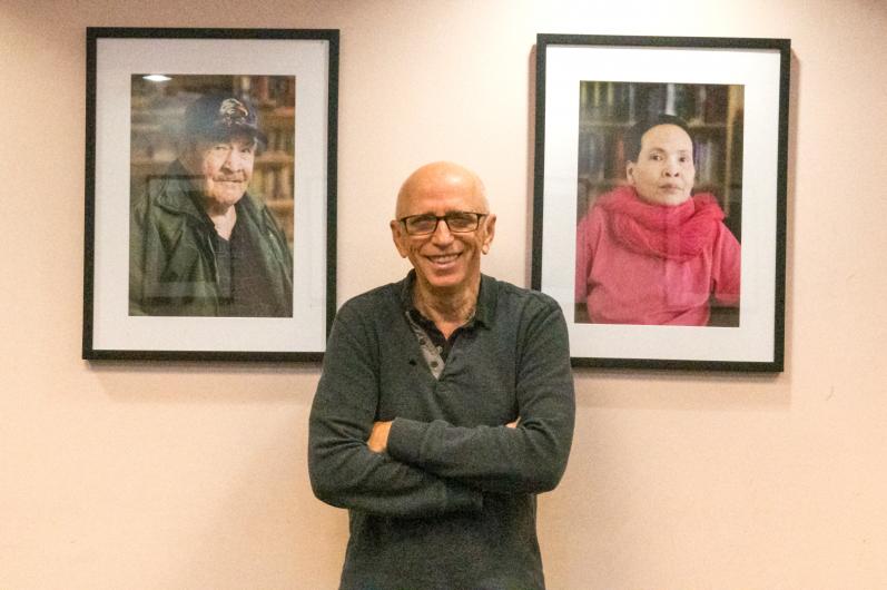 Jim Friesen standing between two portraits of an elderly man and woman who are residents at Central City Lodge in Vancouver.