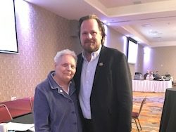 Photo of a man and a woman standing together inside a room with tables covered by white cloths.