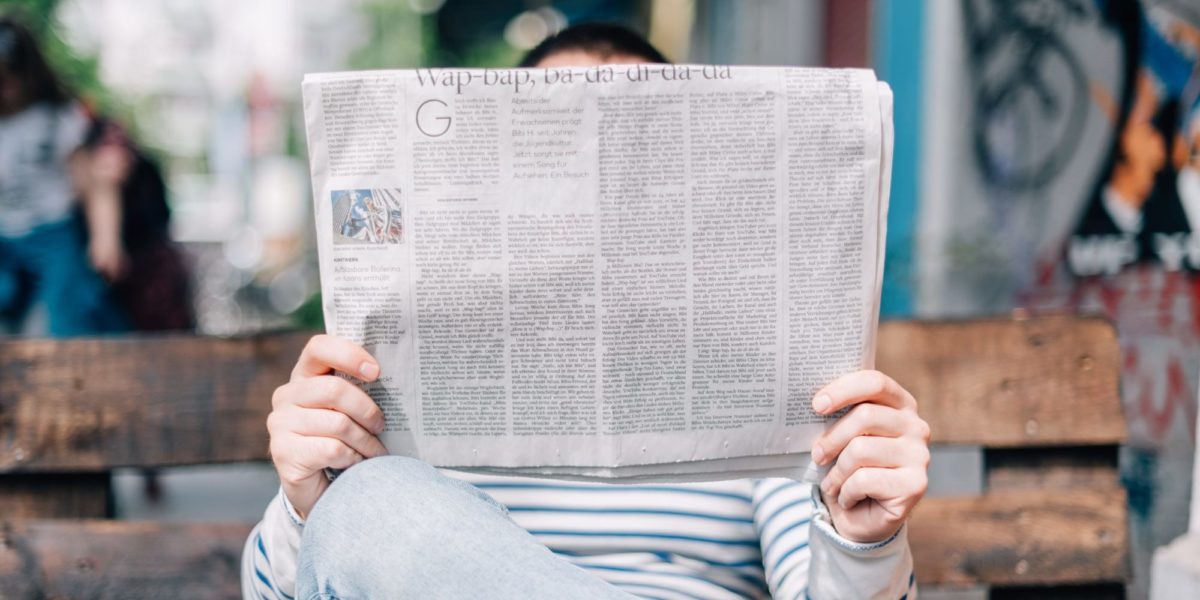 A photo of A person sitting on a bench, reading a newspaper.