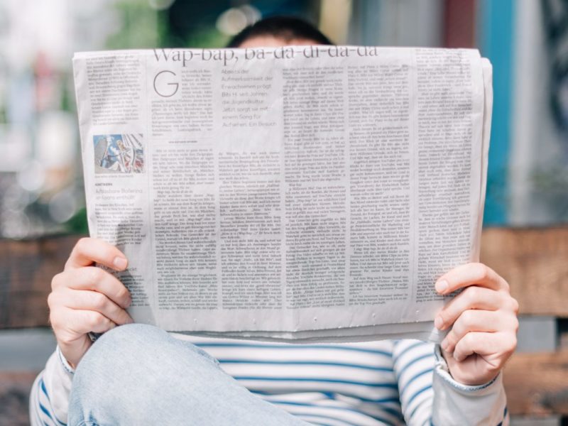 A photo of A person sitting on a bench, reading a newspaper.