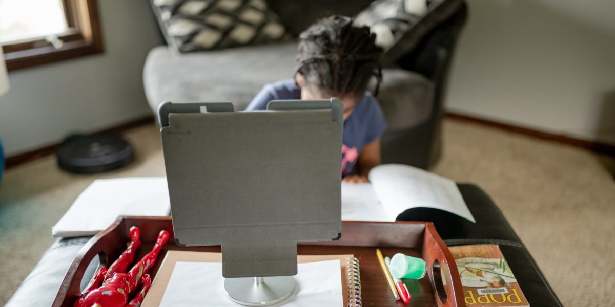 A young girl engages in distance learning from her living room on a tablet.