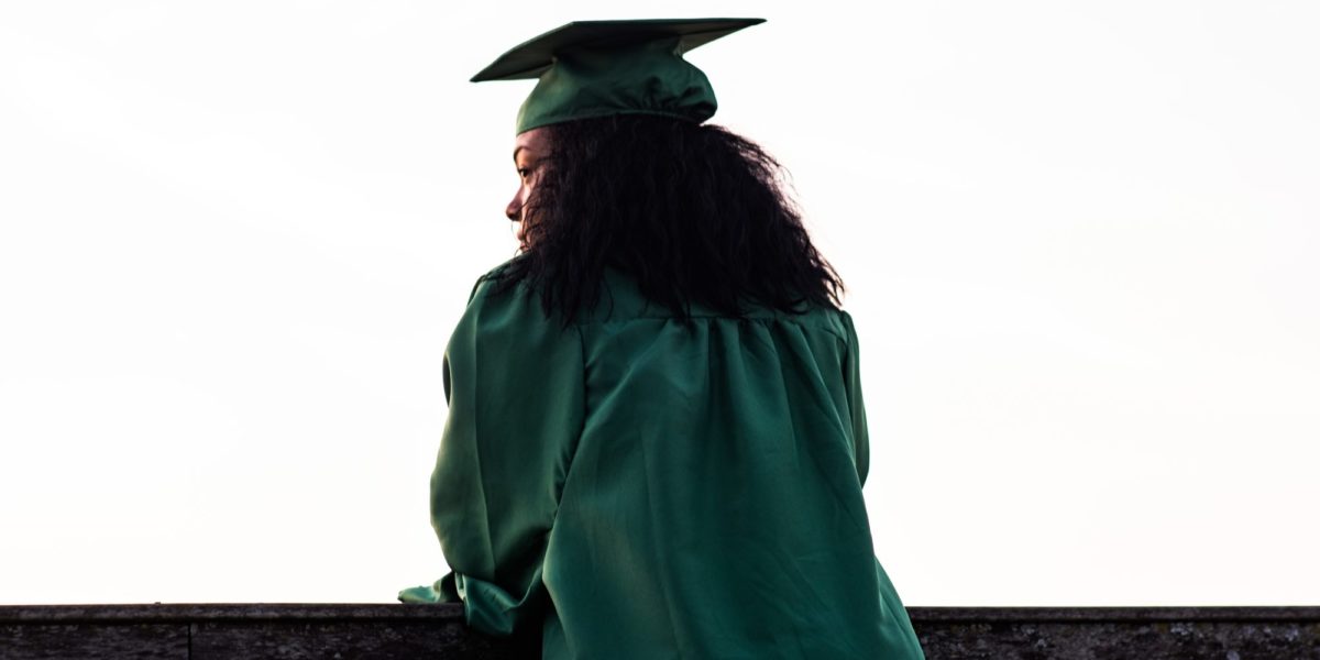 Photo of the shadow of a Black female student in a graduation cap and gown.