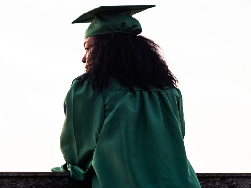 Photo of the shadow of a Black female student in a graduation cap and gown.