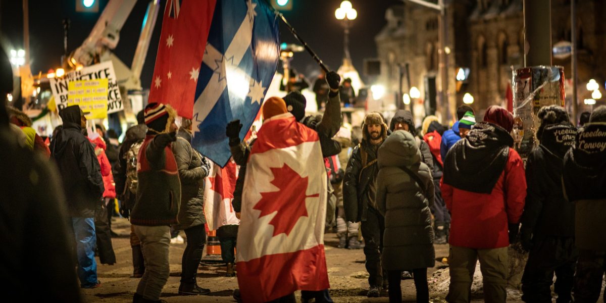 Photo of members of the trucker convoy raise flags and signs in downtown Ottawa.