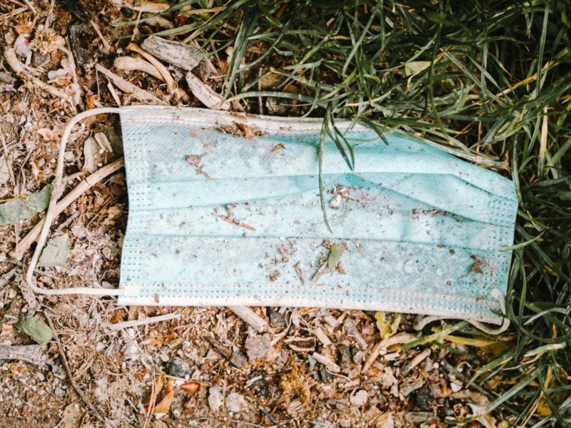 Photo of a surgical mask on the ground in the dirt and grass.