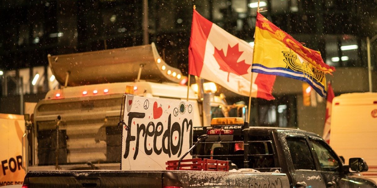 Photo of trucks with Canadian flags and homemade signs attached to their vehicles that read "Freedom"