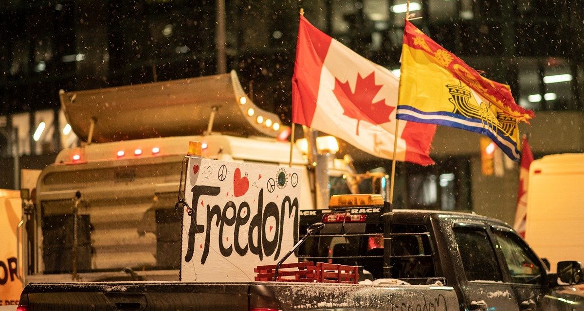 Photo of trucks with Canadian flags and homemade signs attached to their vehicles that read "Freedom"