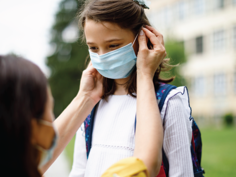 Photo of an adult woman helping a child with a medical facemask