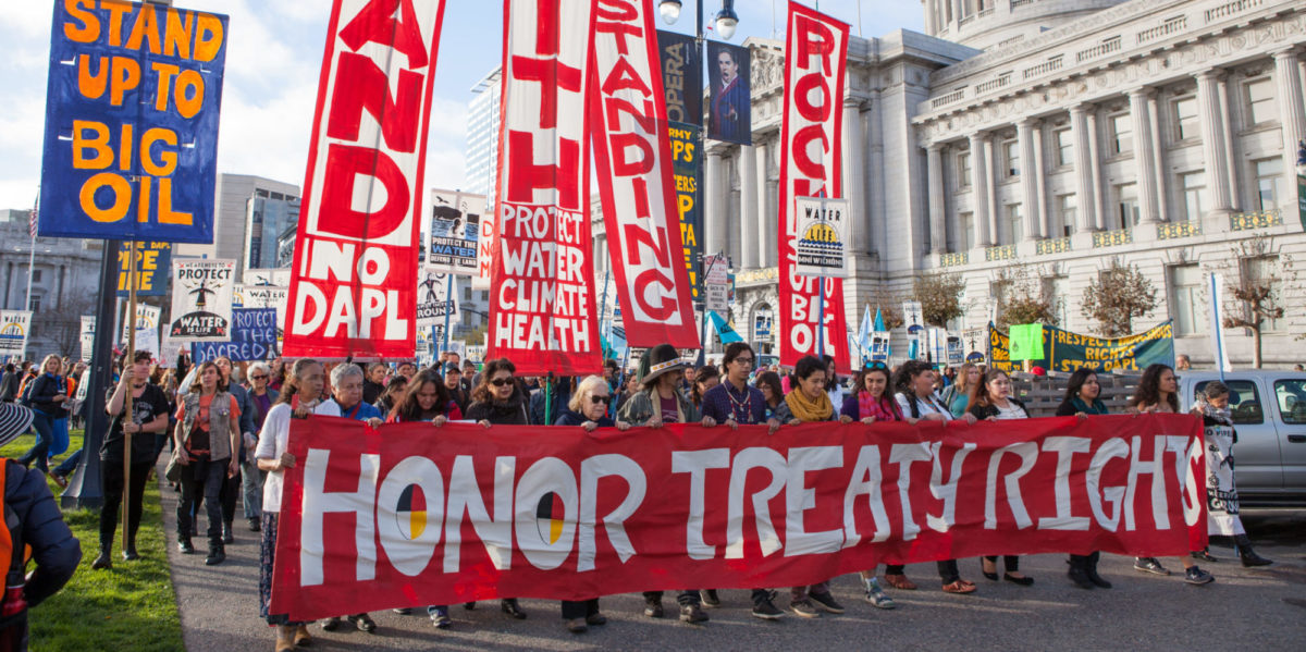 People protesting the Dakota Access Pipeline march past San Francisco City Hall with "Honor Treaty Rights" and other banners.