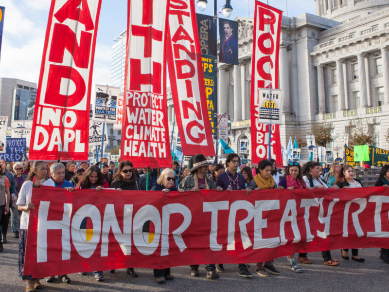 People protesting the Dakota Access Pipeline march past San Francisco City Hall with "Honor Treaty Rights" and other banners.