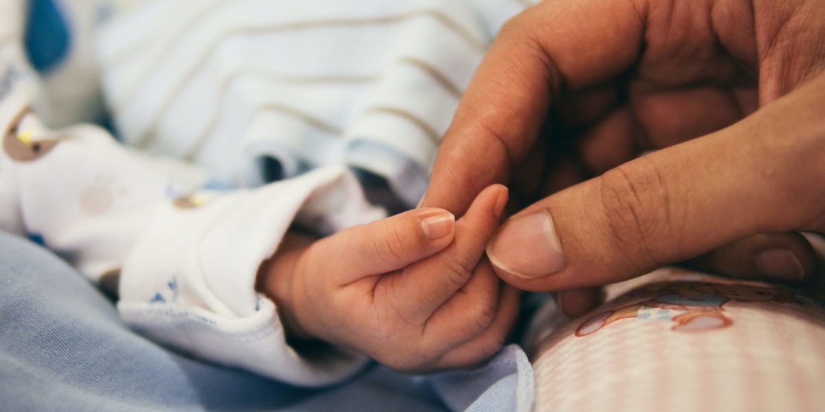 Photo of a newborn baby's hand being held by an adult's fingertips.