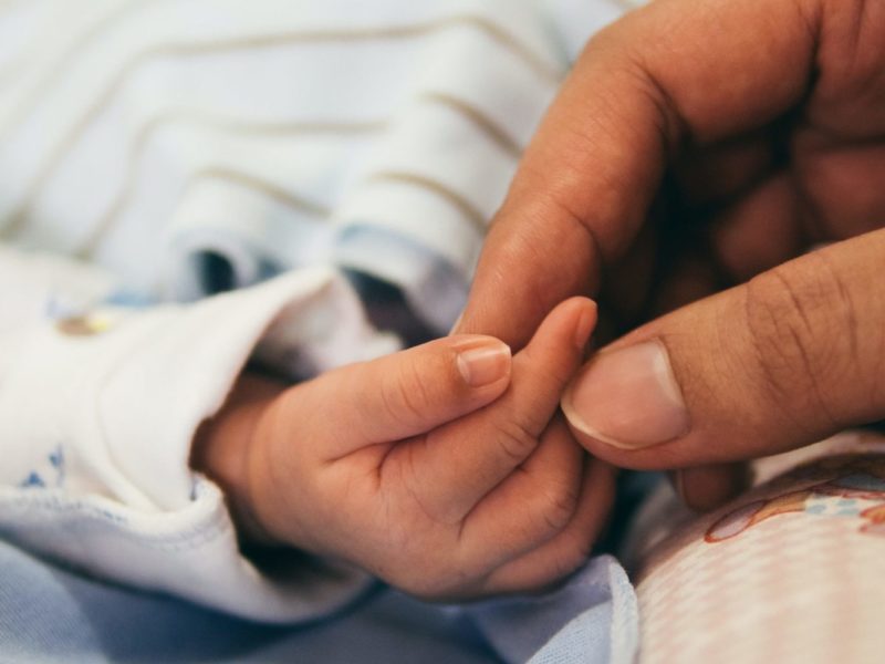 Photo of a newborn baby's hand being held by an adult's fingertips.